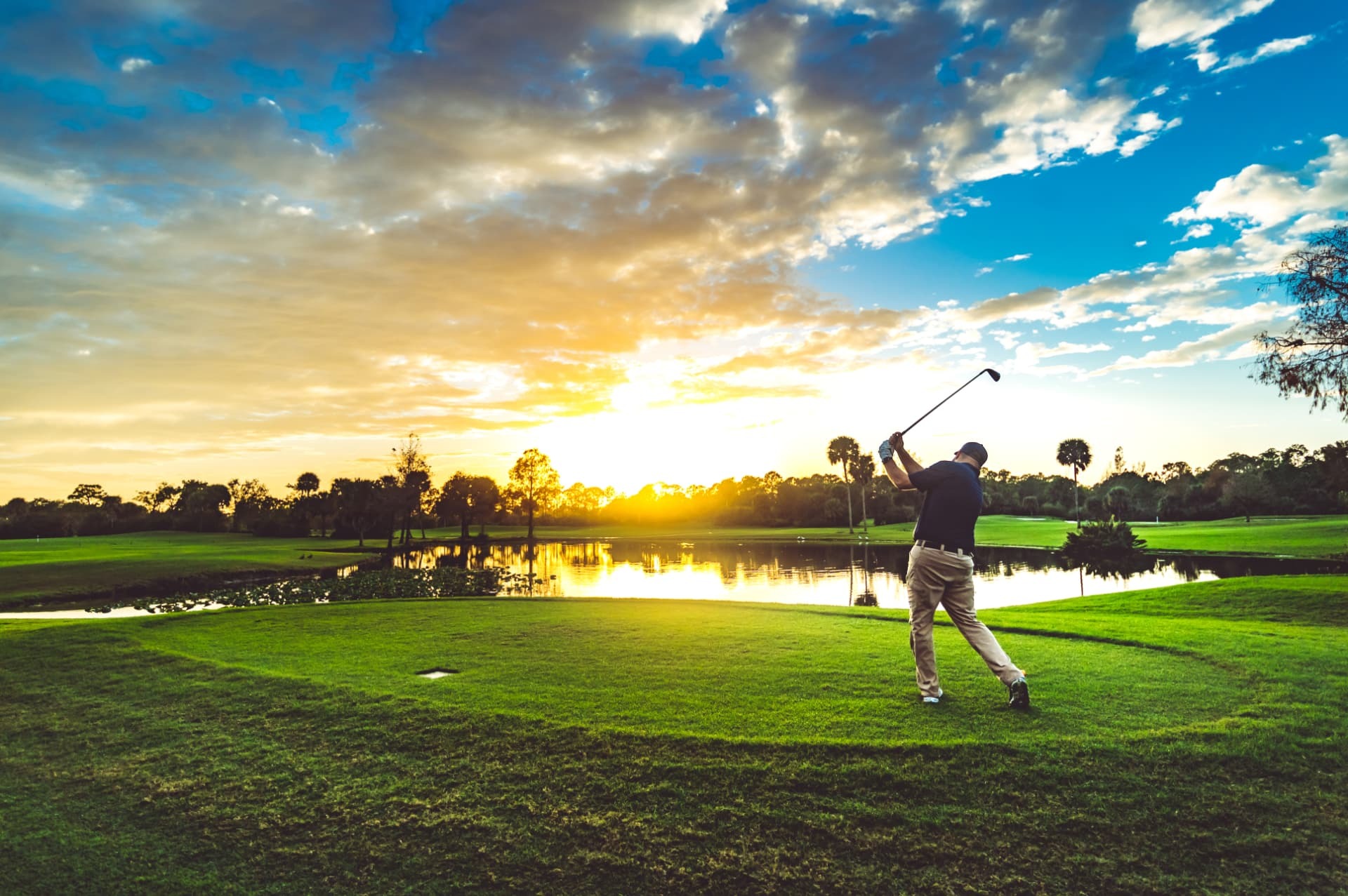 Golfer teeing off beside a lake at sunset